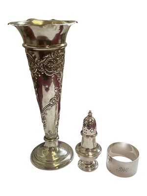Lot 86 - Edwardian silver spill vase with embossed floral scroll decoration, silver napkin ring and a silver pepperette with weighted base (3)