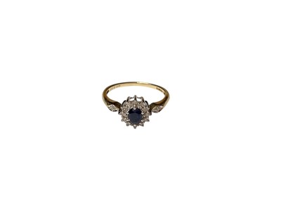 Lot 72 - Sapphire and diamond cluster ring with a central oval mixed cut blue sapphire surrounded by a border of diamonds and further diamond set shoulders in 9ct gold setting