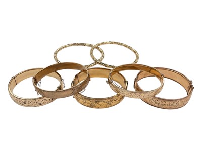 Lot 1053 - Five vintage 9ct gold metal cored hinged bangles with engraved scroll decoration and two other gilt metal bangles