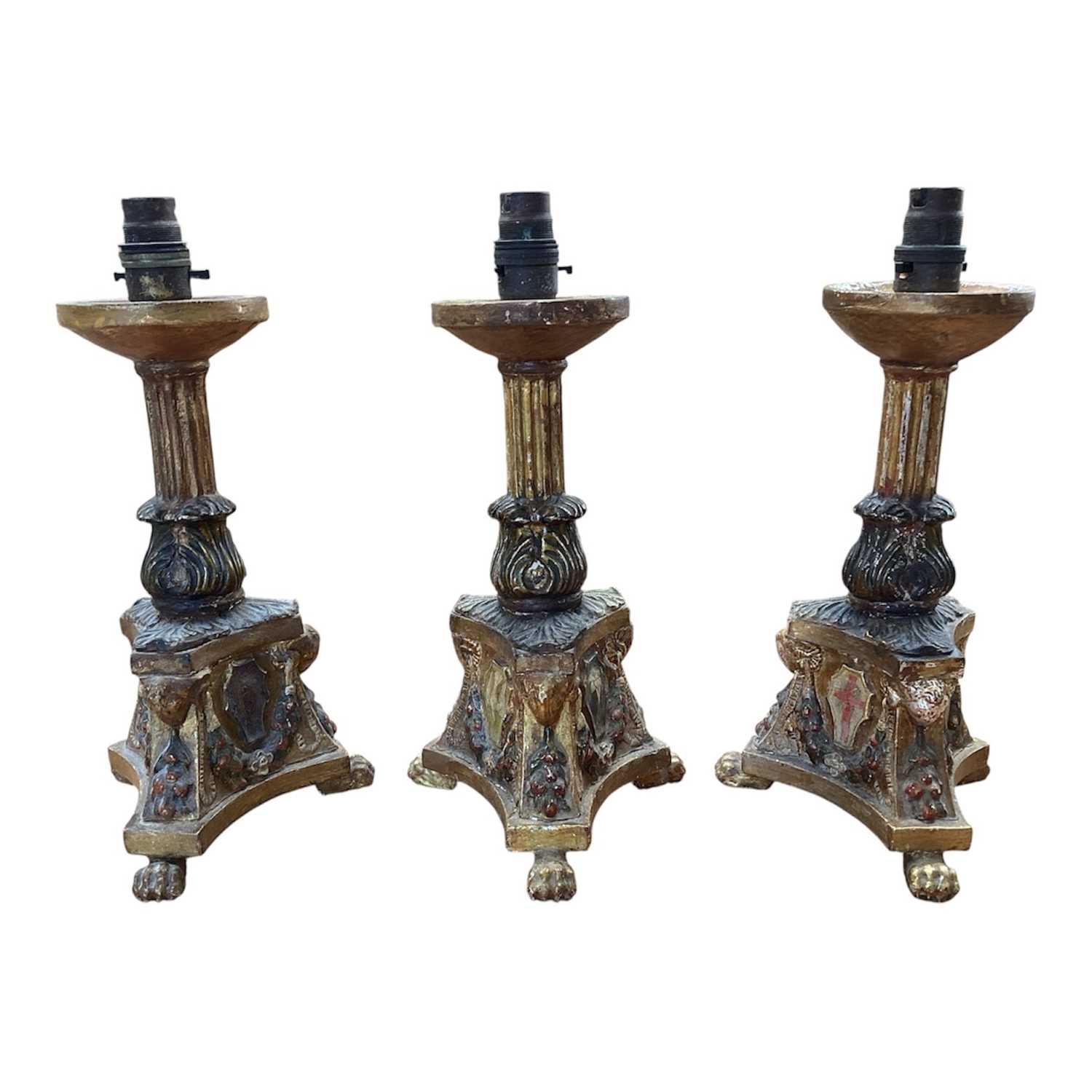 Lot 5107 - Three Italian giltwood and gesso candlesticks, converted to lamps, the central columns supported by shells, on triangular bases with crests, the bases on paw feet, 27.5cm high excluding light fi...