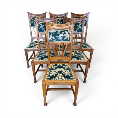 Lot 1495 - Set of six Arts & Crafts golden oak dining chairs, early 20th century, with carved and floral panelled back, floral upholstered seat cushions, on square tapering supports