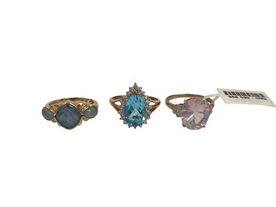Lot 214 - Three contemporary 9ct gold dress rings to include a three stone black opal triplet ring, size M, pear shaped blue topaz and diamond ring, size P½ and a synthetic pink stone and diamond ring, si...