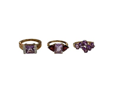 Lot 218 - Three 9ct gold amethyst dress rings to include an amethyst and diamond ring, size P, amethyst and synthetic garnet three stone ring, size M and an amethyst six stone cross-over ring, size M½