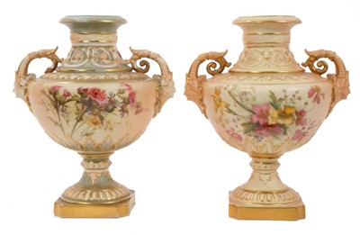 Lot 331 - Two Edwardian Royal Worcester blush ivory ground vases with moulded human mask handles, floral painted decoration on raised socle bases 23cm