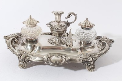 Lot 157 - Victorian silver inkstand of oval form, with shell, scroll and leaf border, central chamberstick with snuffer and a pair of cut glass inkwells with silver mounts, on four scroll feet (London 1891)