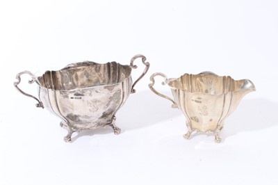 Lot 109 - Edwardian silver two handled sugar bowl with fluted decoration, engraved armorial and scroll handles, raised on four scroll feet, together with a matching milk jug, (Sheffield 1906)