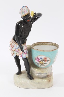 Lot 98 - Late 19th century Dresden figural porcelain sweetmeat, emblematic of Africa, the male figure shown wearing feather headdress and skirt, holding a lemon, the bowl painted with panels of flowers and...