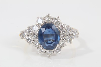 Lot 28 - Sapphire and diamond cluster ring with an oval mixed cut blue sapphire measuring approximately 9.5mm x 7.7mm x 3.3mm surrounded by twelve brilliant cut diamonds with a further six diamonds to the s...