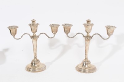 Lot 387 - Pair of Elizabeth II silver three branch candelabra of tapered form with laurel leaf borders, inverted bell shaped candle holders, on domed circular foot, (Birmingham 1962)