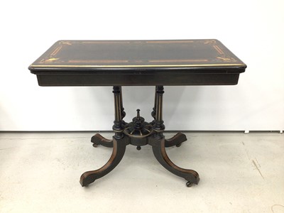Lot 62 - Victorian ebonised and amboyna inlaid card table, with inlaid fold over rounded rectangular top, well below, raised on four columns with gilt fluted ornament and spread supports on castors, united...