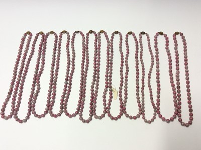 Lot 341 - Collection of twelve Chinese pink hard stone necklaces with round polished beads and oval silver gilt clasps with wire work floral decoration