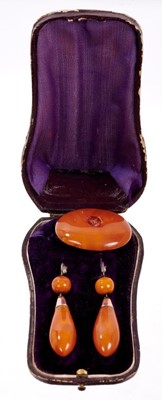 Lot 479 - Victorian amber brooch and earrings, the torpedo shape pendant earrings suspended from a gold mount with coral bead, 60mm, the oval brooch 42mm, all in original fitted box.