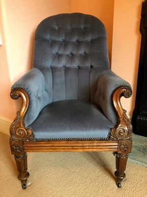 Lot 1430 - William IV rosewood framed easy chair with buttoned blue velvet upholstery, the carved scroll arms and frame on carved and tapered legs terminating on castors