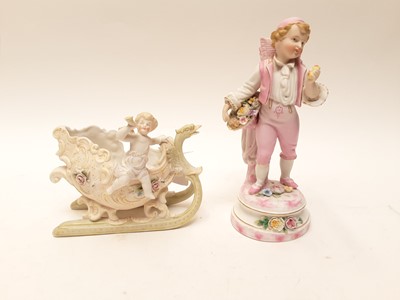 Lot 88 - Bisque porcelain figure of a boy carrying a basket on his back, and a bisque porcelain cherub riding a sledge (2)
