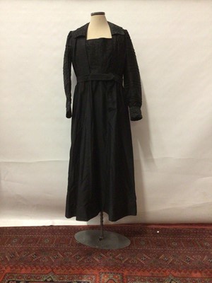 Lot 2063 - Circa 1910 Black dress with flat central panel in bodice and collar, both with lace decoration. Wide pleated sleeves and cuffs.