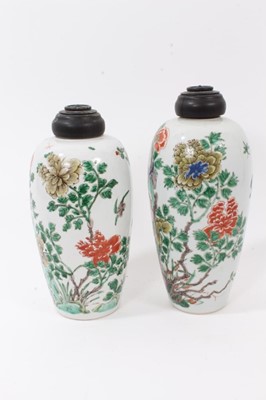 Lot 101 - A near pair of Chinese famille verte ovoid porcelain vases, Kangxi (1662-1722), decorated with flowers, birds and rockwork, with carved wooden covers, one with a double-ring mark to base, 23.5cm an...