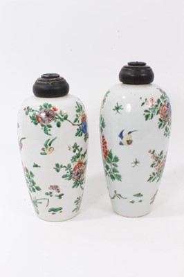 Lot 101 - A near pair of Chinese famille verte ovoid porcelain vases, Kangxi (1662-1722), decorated with flowers, birds and rockwork, with carved wooden covers, one with a double-ring mark to base, 23.5cm an...
