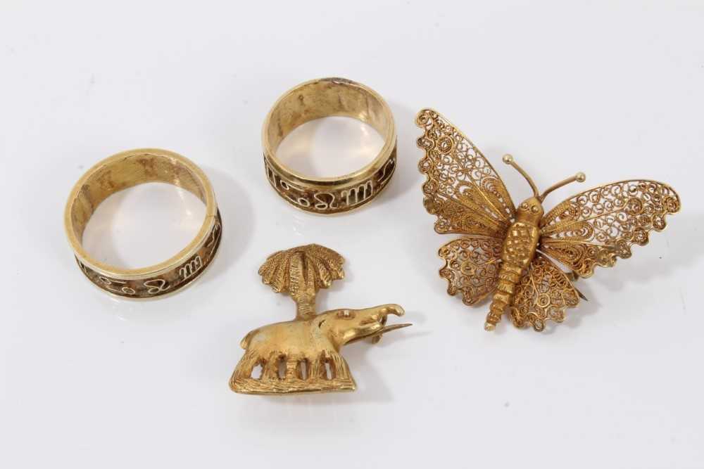 Lot 204 - Two Middle Eastern yellow metal rings, yellow metal elephant palm tree brooch and yellow metal filigree butterfly brooch (4)